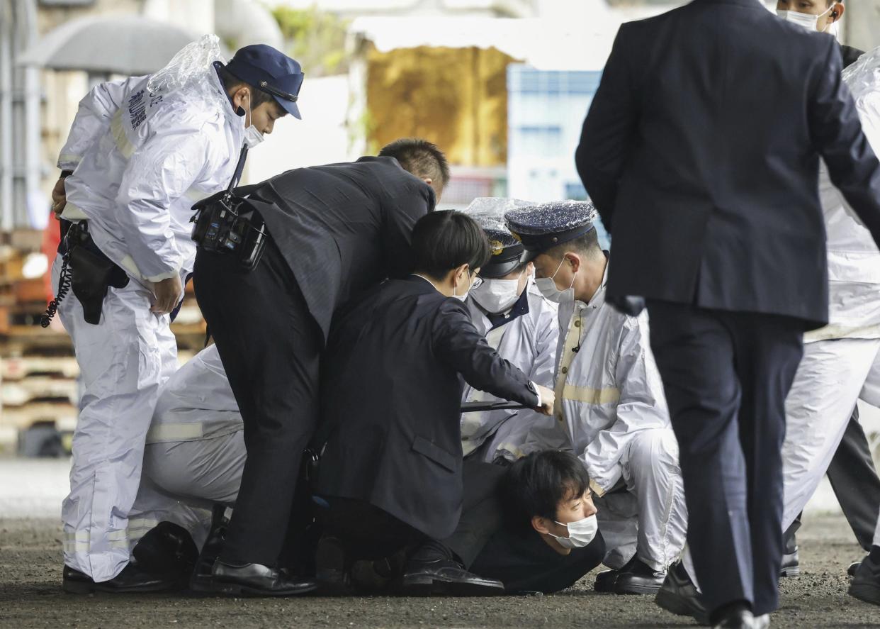 A man believed to be a suspect, center on the ground, is caught by police after he allegedly threw “the suspicious object,” as Japanese Prime Minister Fumio Kishida visited Saikazaki port for an election campaign event in Wakayama, western Japan Saturday, April 15, 2023. Kishida was evacuated unharmed Saturday after someone threw an explosive device in his direction while he was campaigning at the fishing port in western Japan, officials said.(Kyodo News via AP)