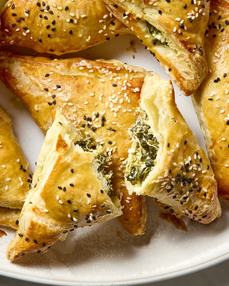 close up shot of spinach and feta bourekas on a plate, with one on top broken open.