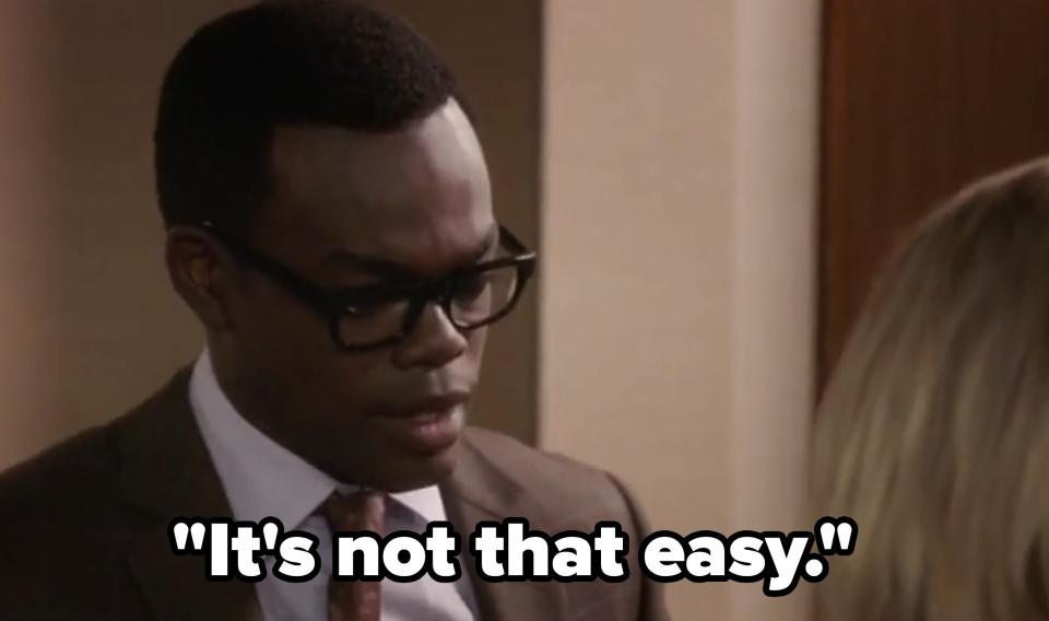 William Jackson Harper, wearing a suit and glasses, is in a scene from "The Good Place" with another unidentified person