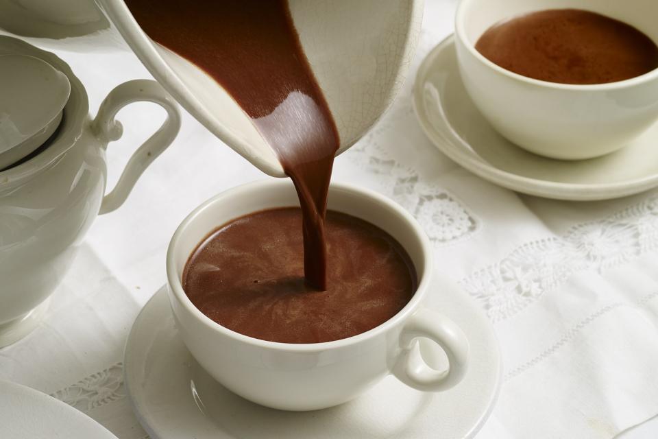 High angle view of pitcher pouring hot chocolate in cup on table