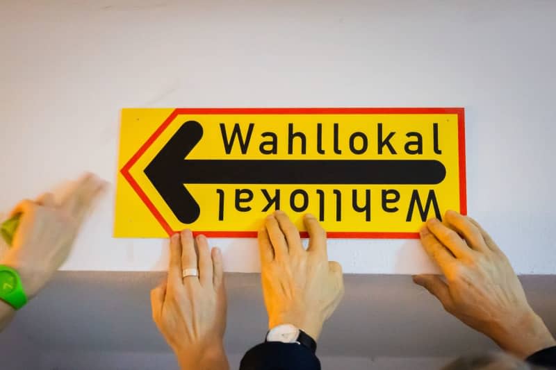 Two poll workers hang a sign at the polling station in the Carl-von-Ossietzky-Gymnasium in Berlin-Pankow before voting begins. Voters in hundreds of Berlin constituencies head to the polls for a partial re-run of the 2021 federal election, after numerous mishaps the first time round. Christoph Soeder/dpa