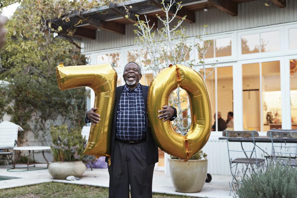 Older adult holds gold balloons with the number 70 in a backyard