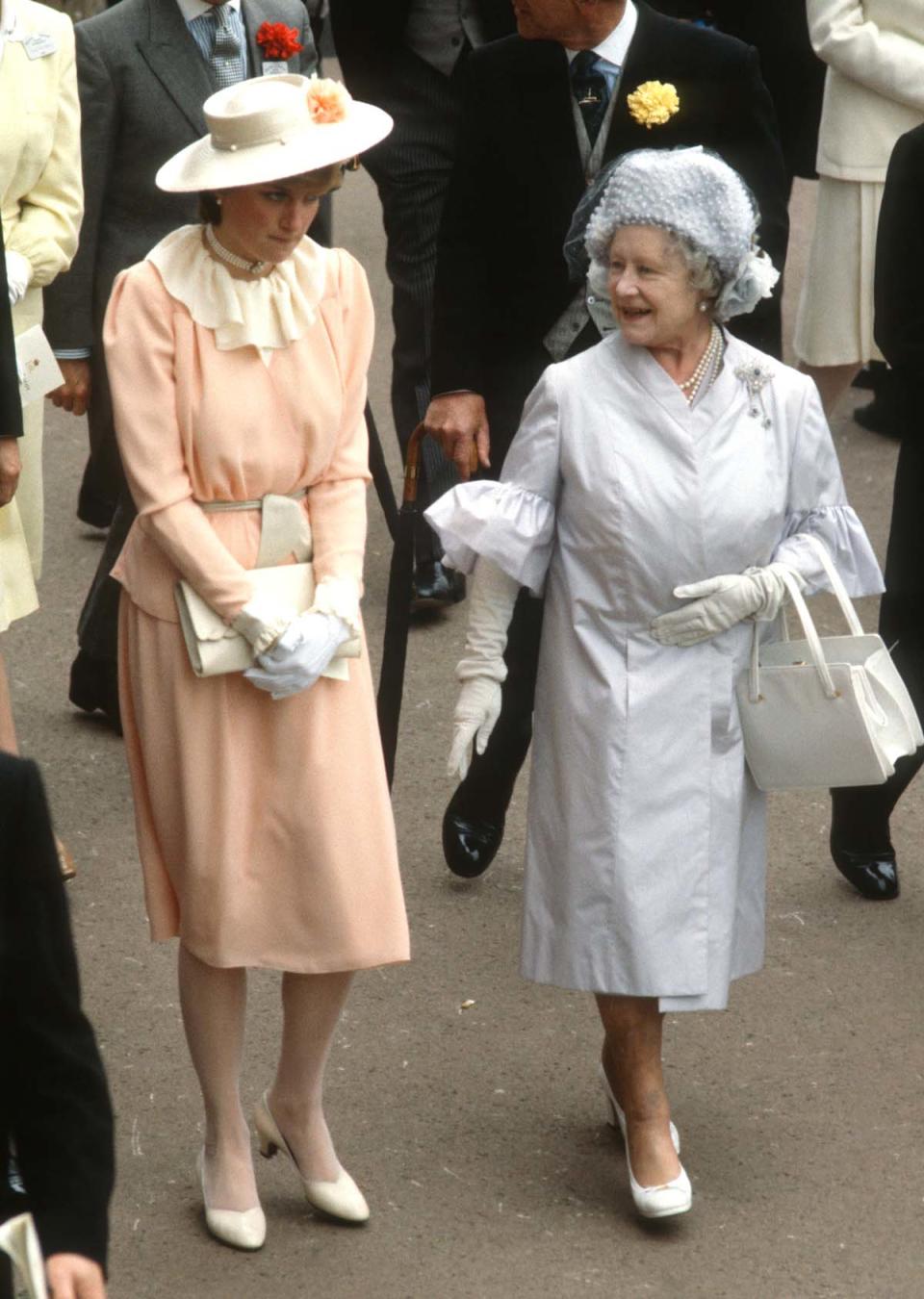 ASCOT, ENGLAND - JUNE 17: Lady Diana Spencer, wearing a peach coloured crepe suit with a wrap top jacket and cream ruffle neck blouse designed by Benny Ong and a yellow straw boater hat with a silk flower, walks next to Queen Elizabeth, The Queen Mother (R) as they attend Royal Ascot on June 17, 1981 in Ascot, United Kingdom. (Photo by Anwar Hussein/Getty Images)