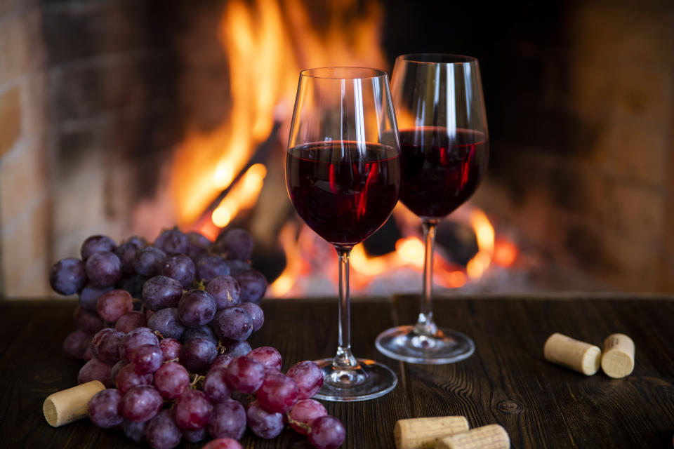 Two glasses of red wine with corks and grapes near the fireplace