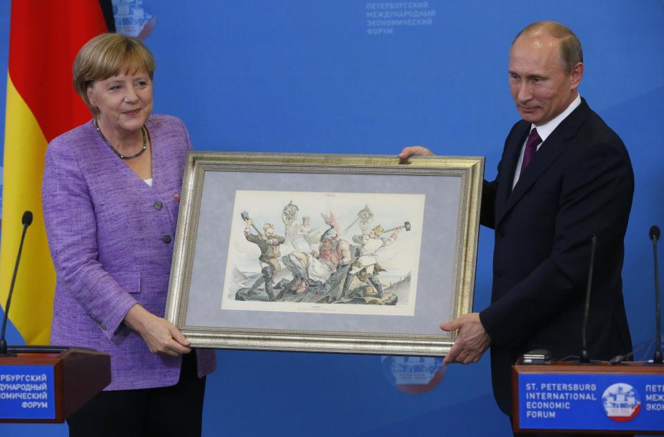Russian President Vladimir Putin, right, hands German Chancellor Angela Merkel an old lithograph dedicated to the signing of a Russian-German trade agreement in 1894 after a news conference at the economic forum in St.Petersburg, Russia, Friday, June 21, 2013. (AP Photo/Dmitry Lovetsky)