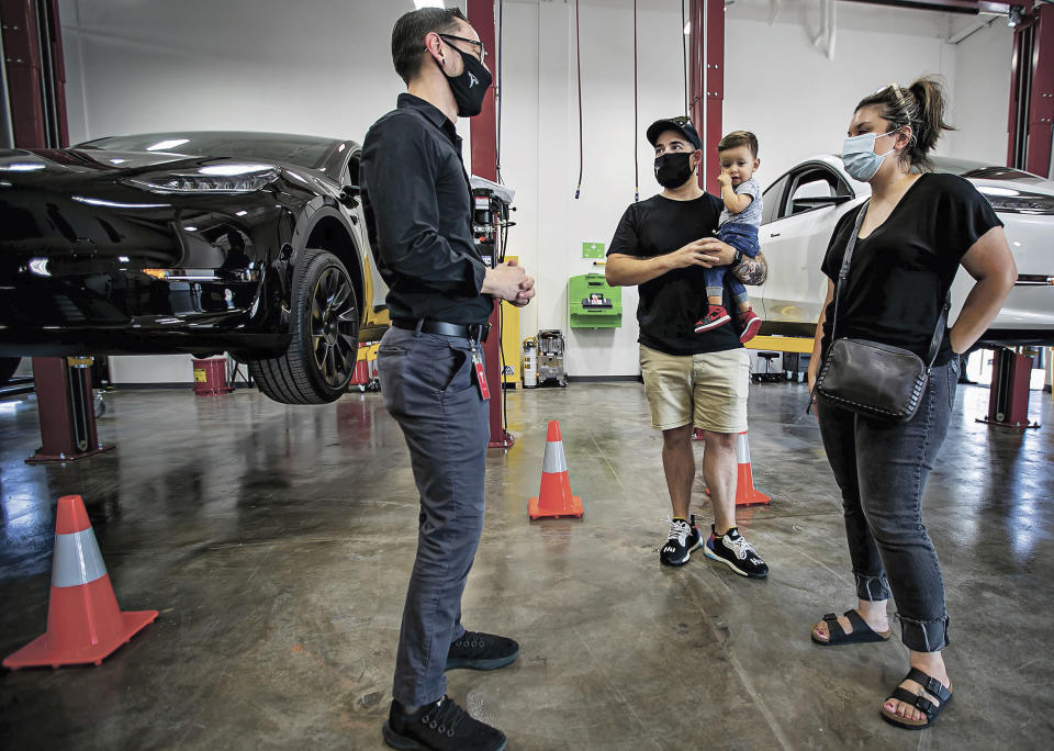 In this Sept. 9, 2021 photo, Tesla owners Joshua Vigil and Melanie Vigil, right, talk with Tesla service manager Brandon Arpin, left, during an event to celebrate a partnership between Tesla and the Nambé Pueblo after the electric car company repurposed a defunct casino into a sales, service and delivery center near Santa Fe, N.M. Tesla has opened a store on tribal land in New Mexico, sidestepping car dealership laws that prohibit car companies from selling directly to customers. (Jim Weber/Santa Fe New Mexican via AP)