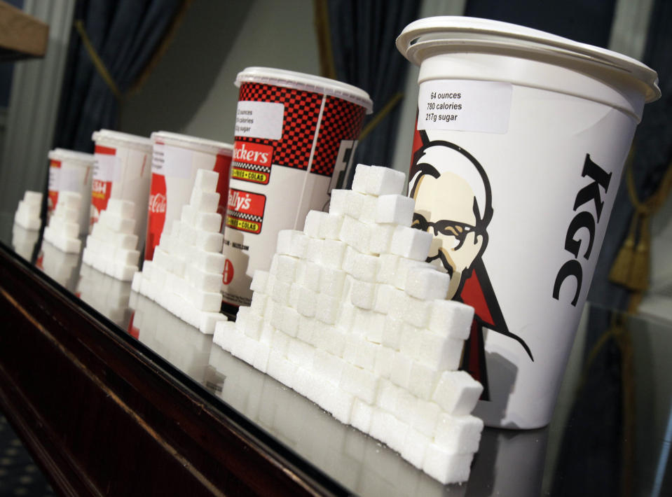 FILE - This Thursday, May 31, 2012 file photo shows a display of various size soft drink cups next to stacks of sugar cubes at a news conference at New York's City Hall. New research greatly strengthens the case against soda and other sugary drinks as culprits in the obesity epidemic. Two major experiments found that children and teens gained less weight when they regularly drank calorie-free beverages instead of sugary ones. A third study gives the first clear evidence that consuming sugary drinks interacts with genes that affect weight. Scientists say the results add weight to the push for taxes, size limits and other policies to curb consumption. (AP Photo/Richard Drew, File)