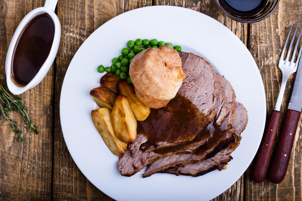 Sunday roast with  roast beef, roast potatoes, green pears, Yorkshire pudding and gravy on rustic wooden table viewed from above, traditional British dish