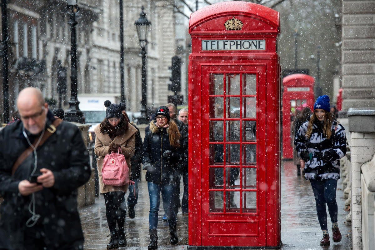 Tourists walk past a red phone box in London as snow falls on Parliament Square (Getty Images)