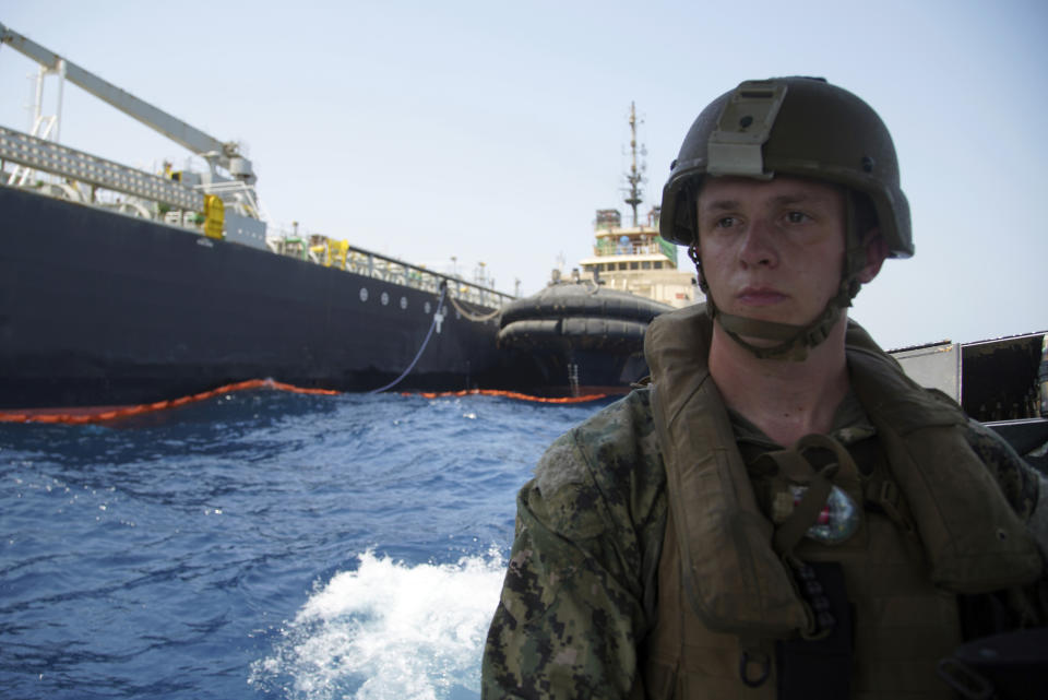 The damaged Panama-flagged, Japanese owned oil tanker Kokuka Courageous, that the U.S. Navy says was damaged by a limpet mine, is seen behind a U.S. sailor, during a trip organized by the Navy for journalists, off Fujairah, United Arab Emirates, Wednesday, June 19, 2019. The limpet mines used to attack the oil tanker near the Strait of Hormuz bore "a striking resemblance" to similar mines displayed by Iran, a U.S. Navy explosives expert said Wednesday. Iran has denied being involved. (AP Photo/Fay Abuelgasim)