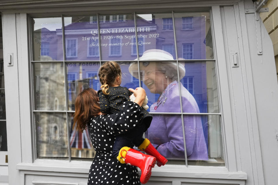 Kate Castang lifts up her 2 year-old daughter Cleo to show her a picture of the late Queen Elizabeth II in Windsor, England, Thursday, Sept. 15, 2022. The Queen will lie in state in Westminster Hall for four full days before her funeral on Monday Sept. 19. (AP Photo/Gregorio Borgia)