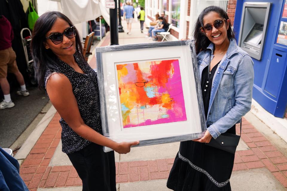 Two visitors hold up a piece of artwork on display during Artisphere 2022