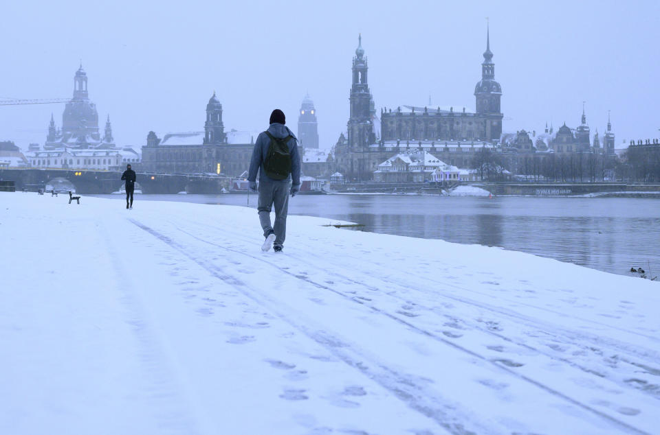 Passers-by walk through the snow in the morning on the banks of the Elbe river against the backdrop of the old town in Dresden, Germany, Sunday, Feb. 7, 2021. (Sebastian Kahnert/dpa via AP)