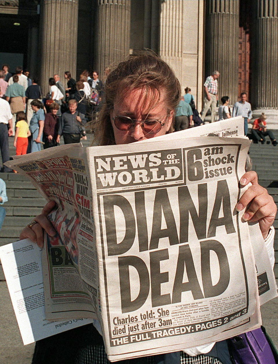 Person reads newspaper headline about Princess Diana's death outside a building with steps and columns, conveying the news' impact