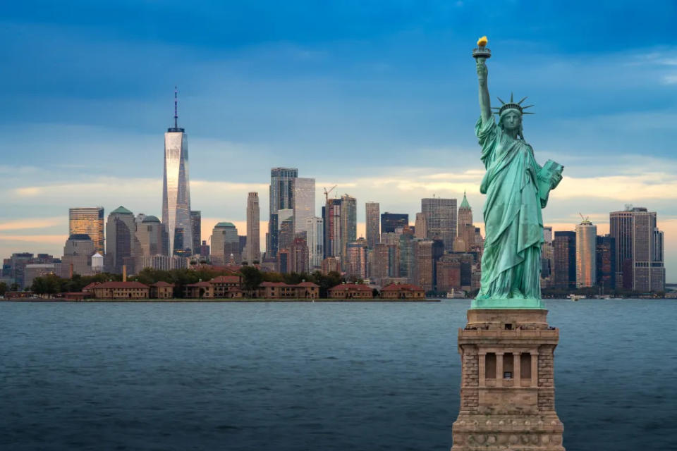 The statue of Liberty with Downtown New York skyline panorama with Ellis Island via Getty Images