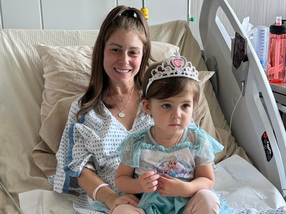 Jillian Breslin lying on a bed in the hospital with her toddler sitting on her lap.