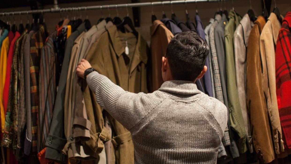  Young man looking through clothes rail in vintage shop. 