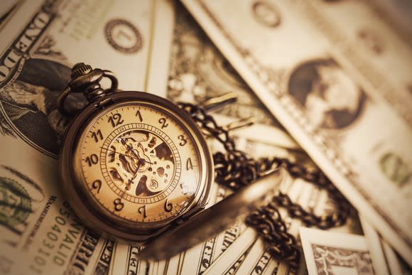 Old-style pocket watch on a chain sitting atop paper currency