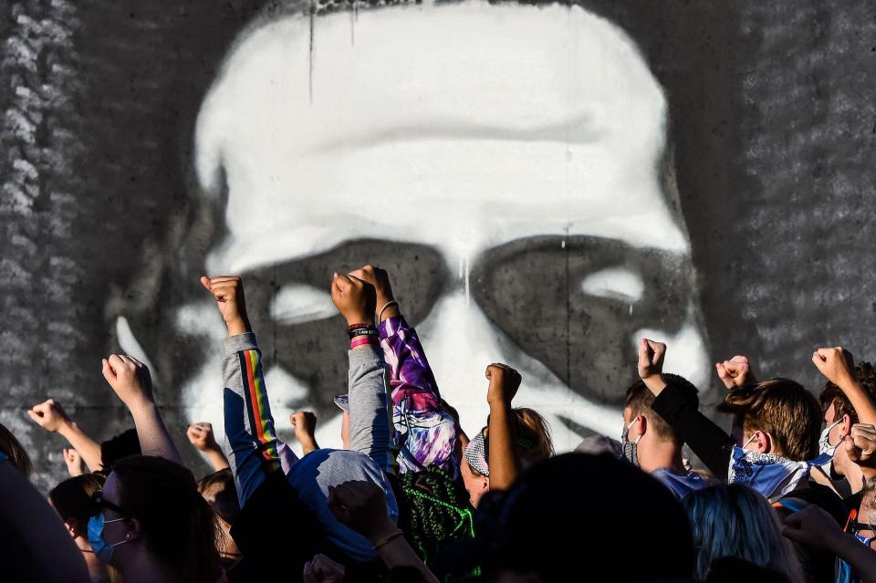 Protestors raise their fists by a George Floyd mural