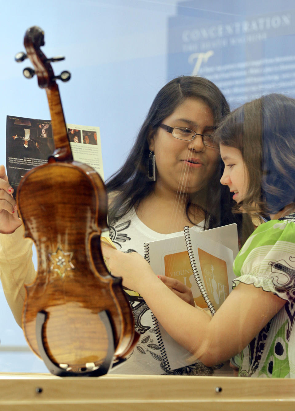 In a Monday, April 9, 2012 photo, Dayani Sanchez, 12, left, and Kathryn Dull, 11, right, talk about the Violins of Hope exhibit at UNC Charlotte in Charlotte, N.C.. Eighteen violins recovered from the Holocaust and restored by Israeli violin maker Amnon Weinsten make their U.S. debut on Sunday, April 15. Some were played by Jewish prisoners in Nazi concentration camps, while others belonged to the Jewish Klezmer musical culture. (AP Photo/Chuck Burton)