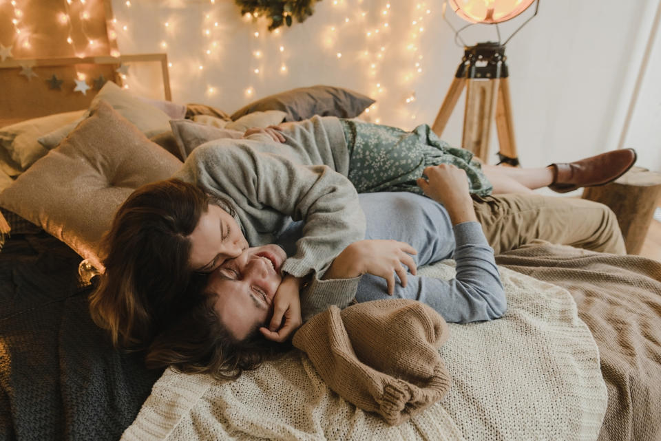 A beautiful young smiling woman with long hair with a handsome young smiling man lies on the bed in sweaters, laughing, hugging, kissing.