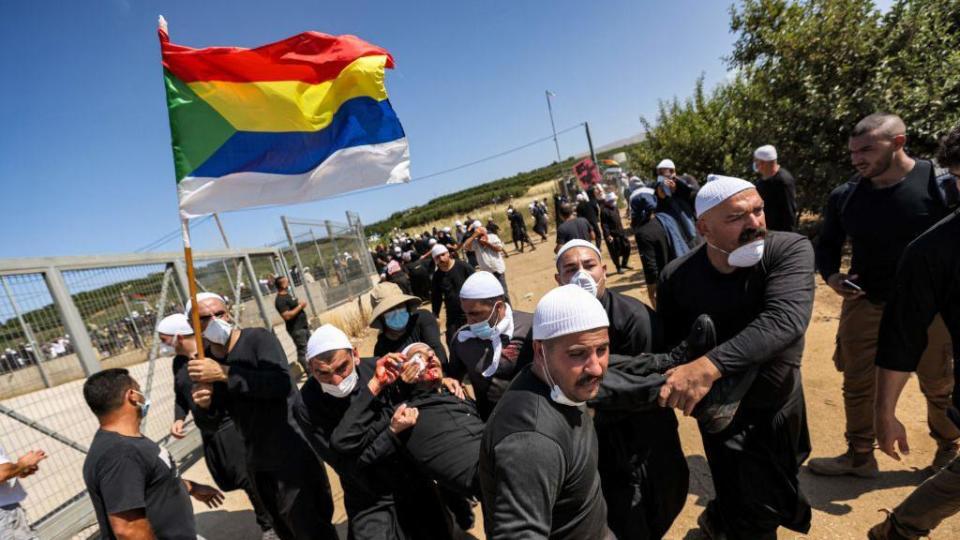 Un miembro de la comunidad drusa sostiene su bandera mientras lleva a un manifestante herido durante una protesta en el pueblo de Majdal Shams en los Altos del Golán anexados por Israel el 21 de junio de 2023, contra un proyecto de turbinas eólicas israelíes supuestamente planeado en tierras agrícolas del pueblo.