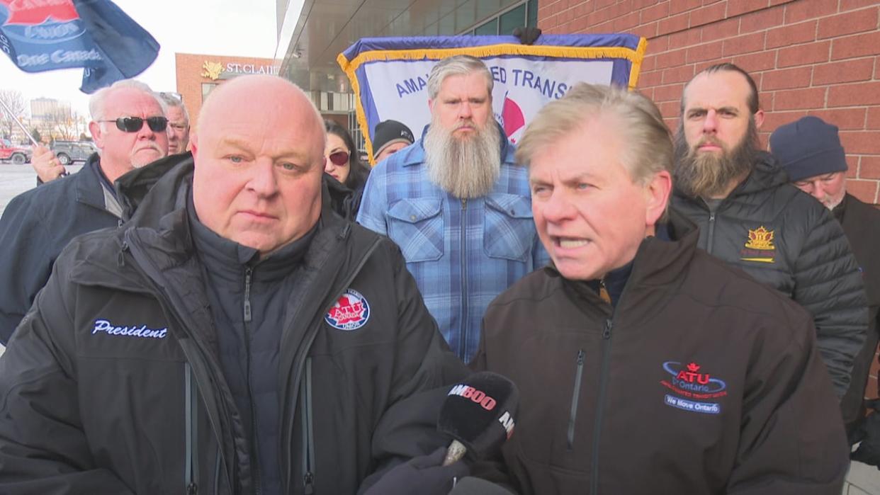 John Di Nino (left), Canadian president of the Amalgamated Transit Union, and Manny Sforza (right), international president of the union, address media in front of the bus terminal in downtown Windsor on Jan. 16, 2024. Windsor bus operators represented by ATU stand behind them. (Chris Ensing/CBC - image credit)