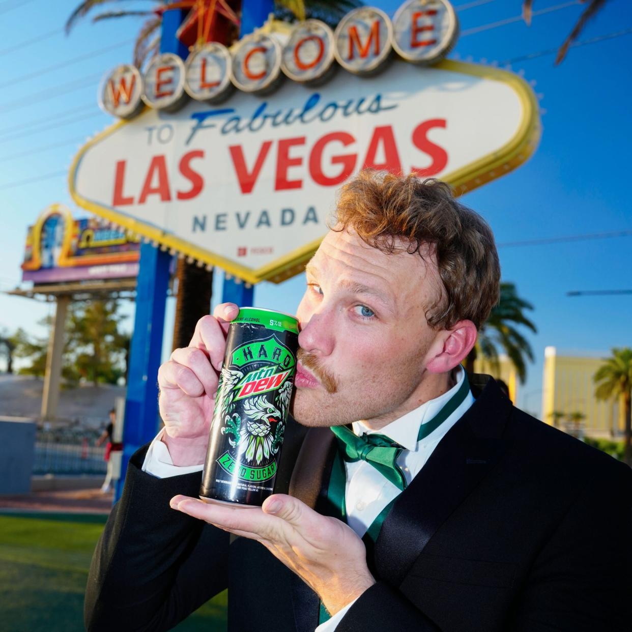 Thomas Rank kisses a can of Hard Mtn Dew in front of the Welcome to Las Vegas sign