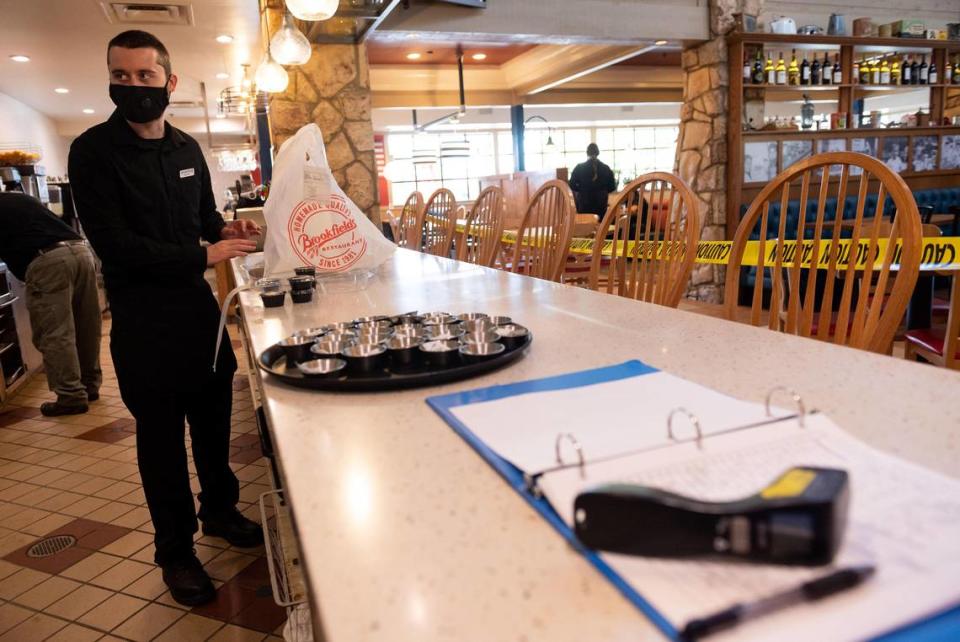 A thermometer used to check employees temperatures sits on the counter with a sign-in form to confirm they were not exposed to the coronavirus at Brookfields Restaurant in Roseville as host Devin Huddleston trains on up-to-date safety protocols on the second day of dine-in service, Friday, May 15, 2020, after the restaurant reopened.