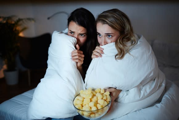 Two young women hide beneath a blanket