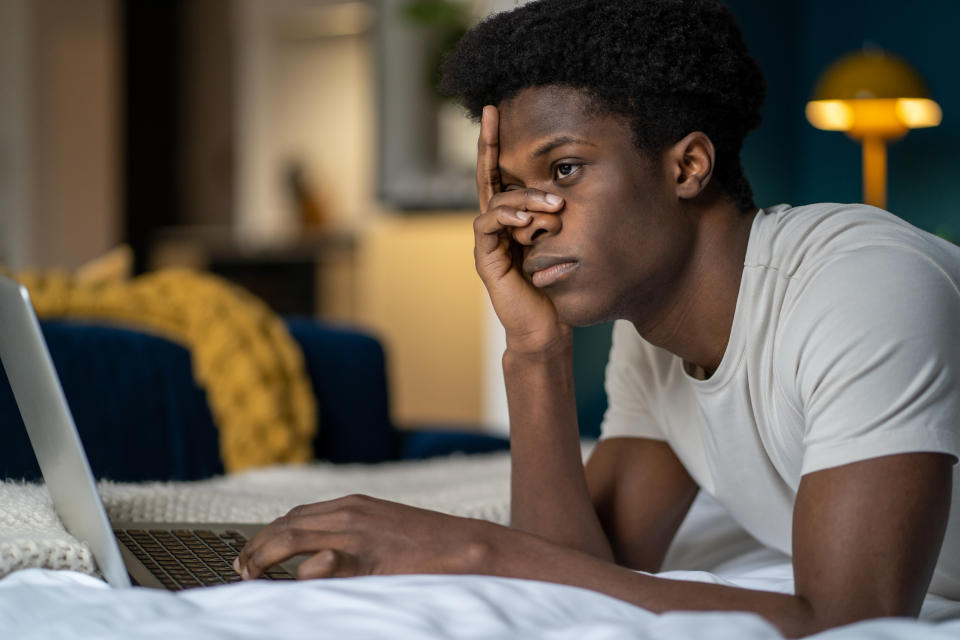 Person looking thoughtful while using a laptop in a bedroom setting