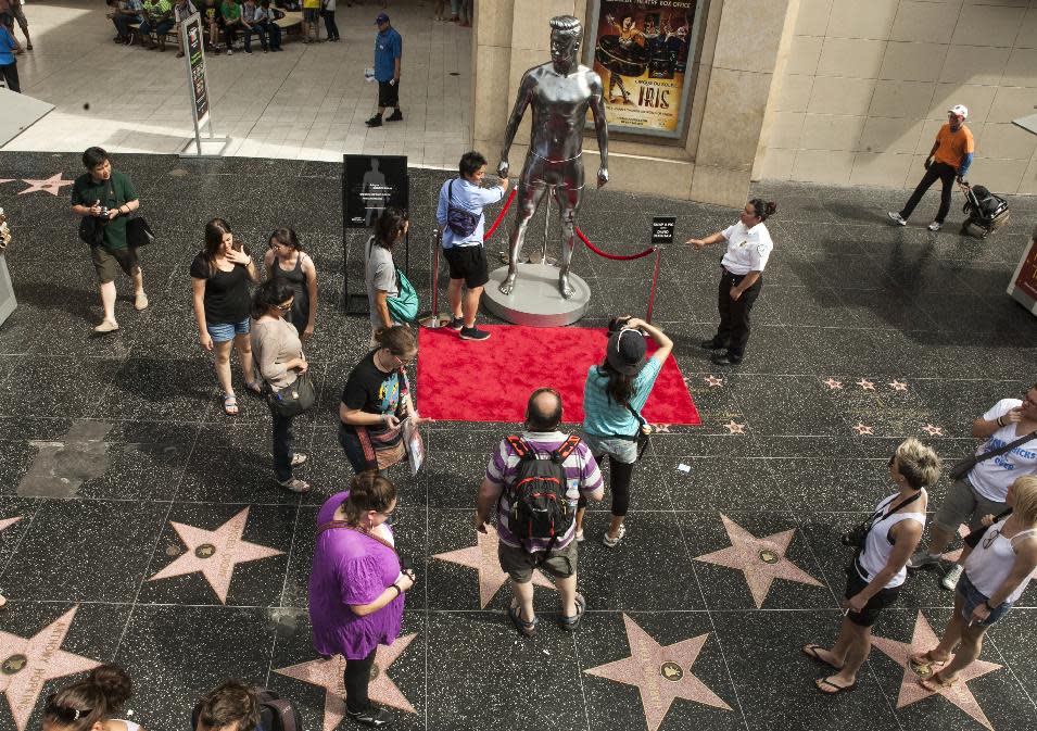 FILE - In this file photo taken Aug. 17, 2012, tourists take photos with a 10-foot statue created and modeled after English soccer star David Beckham displayed in the Hollywood section of Los Angeles. The intersection of Hollywood and Highland is the crossroads for the Hollywood Walk of Fame, where more than 2,400 terrazzo-and-brass stars containing the biggest names in the entertainment business can be viewed by just walking down the sidewalk. (AP Photo/Damian Dovarganes, File)