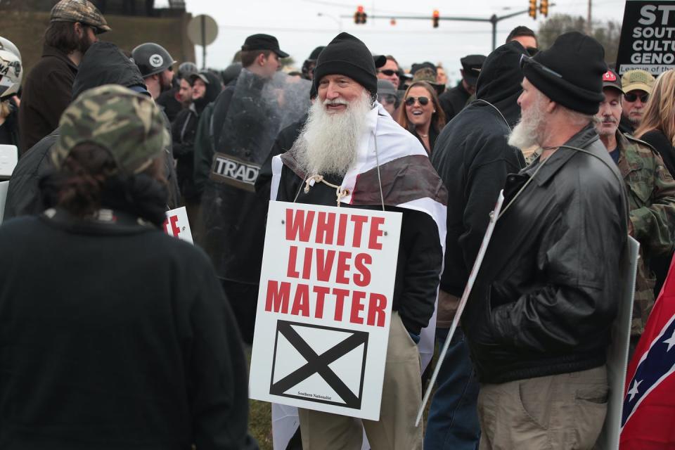 Bearded older man at a white supremacist rally carrying a sign that says 'White Lives Matter'