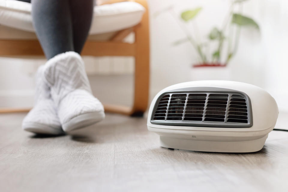 Close up of electric heater in room and woman's feet with slippers on the background