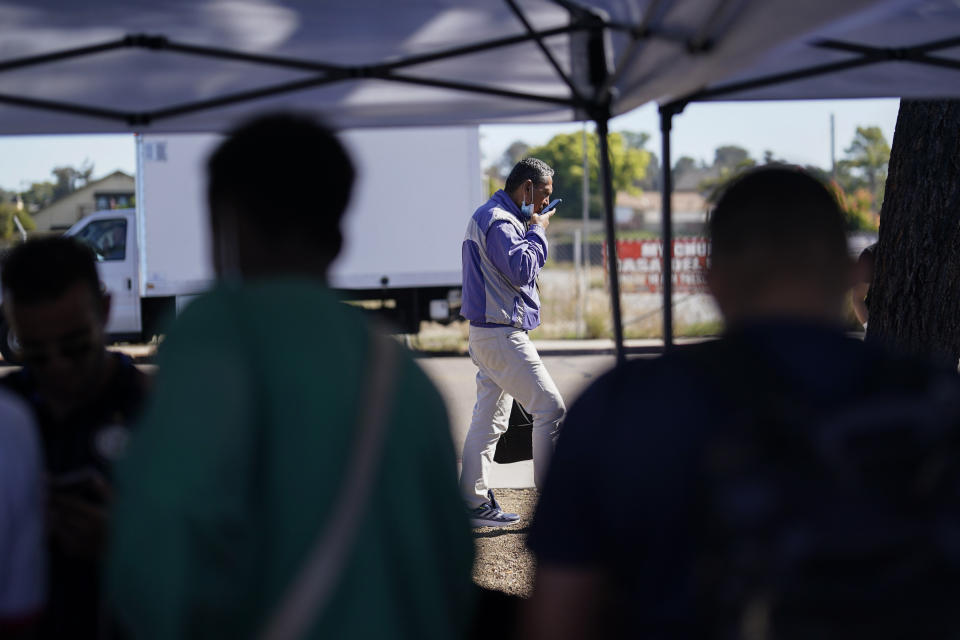 A migrant talks on a phone in a parking lot set up to help people with travel plans, accommodation, food and shelter, Friday, Oct. 6, 2023, in San Diego. San Diego's well-oiled system of migrant shelters is being tested like never before as U.S. Customs and Border Protection releases migrants to the streets of California's second-largest city because shelters are full. (AP Photo/Gregory Bull)