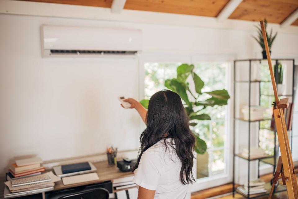 woman in home office using remote control to turn on air conditioner mounted on wall