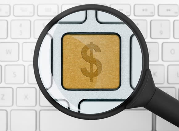 Magnifying glass highlighting a golden dollar-sign key on an otherwise plain, white, and unremarkable computer keyboard.