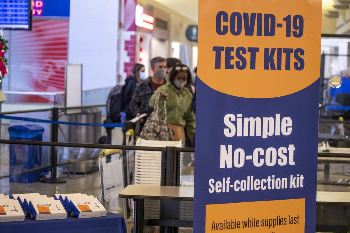 Travelers go through a security checkpoint near a display of free COVID test self-collection kits at John Wayne Airport in Santa Ana, Calif.