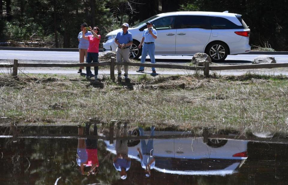 Visitors from China photograph the waterfalls as seepage from the Merced River floods a meadow, foreground, Friday, April 28, 2023 in Yosemite Valley.