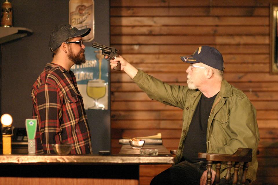 A frustrated regular, played by Carl Hunnell, holds a gun to the bartender's head as both prepare for the end of the world during the play "Early One Evening at the Rainbow Bar and Grill." Aaron McNulty plays the bartender.
