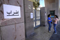 Lebanese women stand next of an Arabic placard that reads: "Strike," at the main entrance of the Lebanese education ministry, in Beirut, Lebanon, July 27, 2022. Tens of thousands of Lebanese public sector workers are on strike for a sixth week as they struggle to cope with the country's crippling economic crisis. (AP Photo/Hussein Malla)