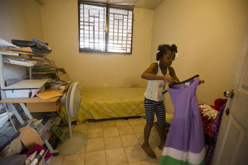 Franchina 11, decides on a graduation ceremony dress in her bedroom at her foster parents' home in Port-au-Prince, Haiti on Saturday, June 30, 2018. In her orphanage, she shared a bunkroom with many other children. Now Franchina has a bedroom to herself. (AP Photo/Dieu Nalio Chery)