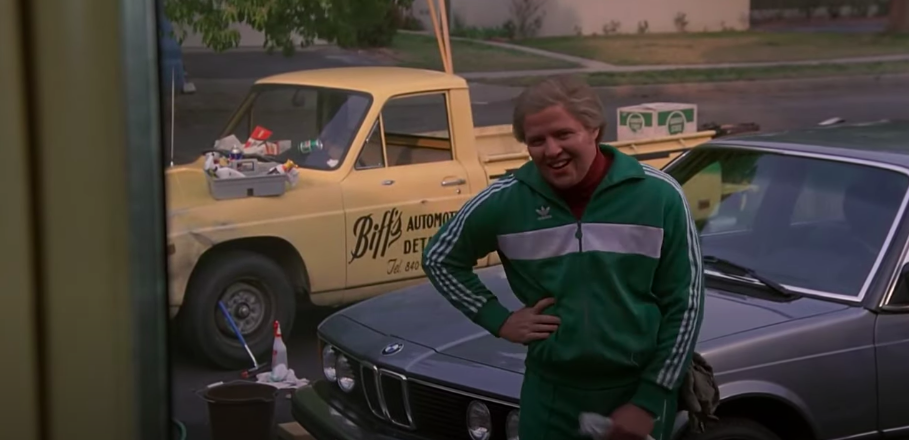 A man stands outside in a driveway, polishing cars