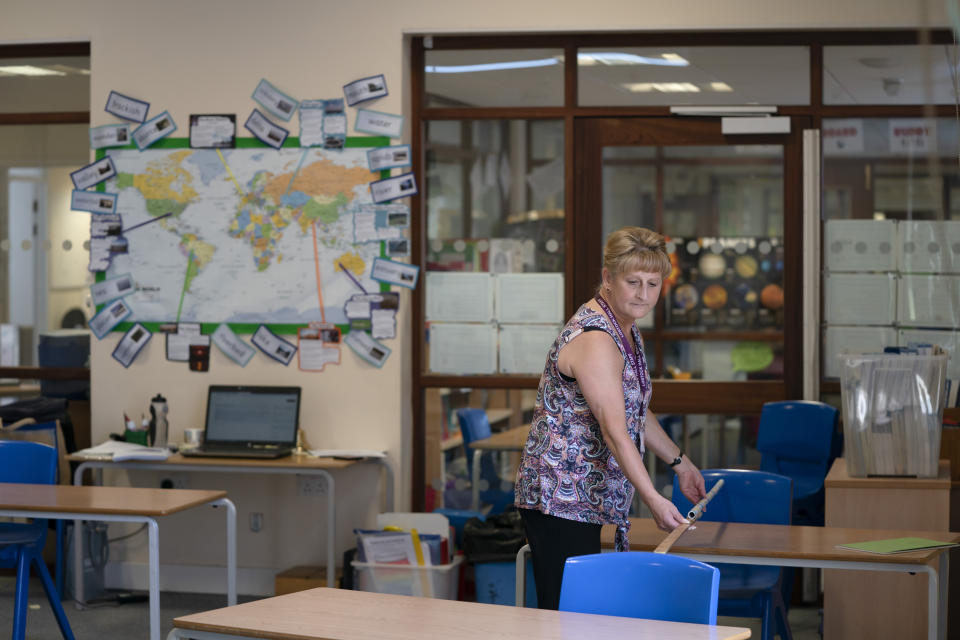 Year 6 teacher Jane Cooper uses a 2 meter length of ruler and pipe to check seat spacings in her classroom as measures are taken to prevent the transmission of coronavirus before the possible reopening of Lostock Hall Primary school in Poynton near Manchester, England, Wednesday May 20, 2020. ( AP Photo/Jon Super)