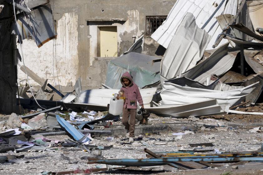 A Palestinian child walks past factories destroyed in the Israeli bombardment of the Gaza Strip in Deir al Balah on Saturday, Jan. 13, 2024. (AP Photo/Adel Hana)