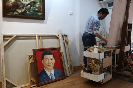 Chen Jingyang, who has been in the village for 12 years, works on his original painting as a portrait of the Chinese president Xi Jinping by him is placed on the ground at his studio in Dafen Oil Painting Village in Shenzhen, Guangdong province, China December 6, 2018. REUTERS/Thomas Suen/Files
