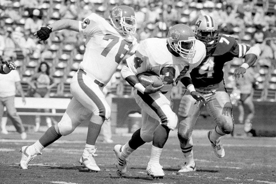 FILE - New Jersey Generals Herschel Walker, center, carries the ball for a first down past General's Bryan Millard, left, and Los Angeles Express' Dennis Edwards during the first quarter of an USFL game in Los Angeles on March 6, 1983. The original USFL was a league that made a whole lot of sense, only to be undone by the greed and hubris of owners such as former President Donald Trump, who saw the fledgling organization as a conduit to the NFL. (AP Photo/File)