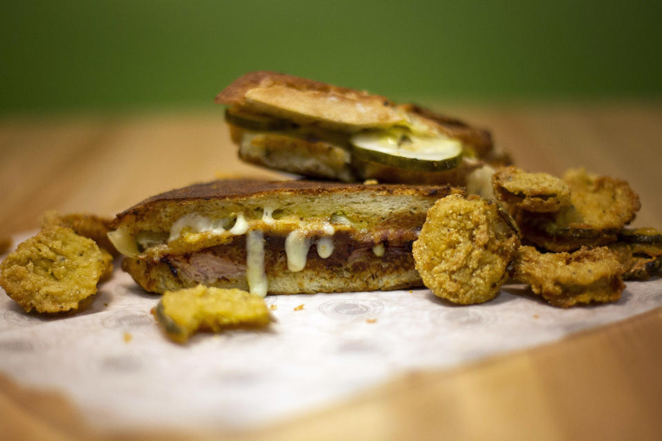 In this Wednesday, Nov. 14, 2012 photo, two items from the menu, a Cuban sandwich and fried pickles, appear on display at the Food Network Kitchen, at the Fort Lauderdale-Hollywood International Airport, in Fort Lauderdale, Fla. Dining-on-the-go is soaring at the airport where travelers can dine at a restaurant inspired by a test kitchen. (AP Photo/J Pat Carter)