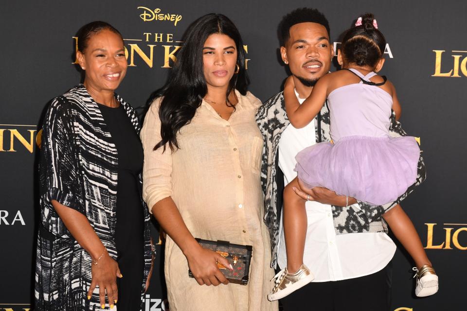 Three people at 'The Lion King' premiere; a man holds a child, and two women stand beside them, dressed in smart attire