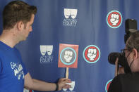 Workers who help bring Disneyland's beloved characters to life take a picture with the logo of the Actor Equity Association, after announcing they've collected enough signatures to support their push for a union doing a news conference in Anaheim, Wednesday, April 17, 2024. (AP Photo/Damian Dovarganes)